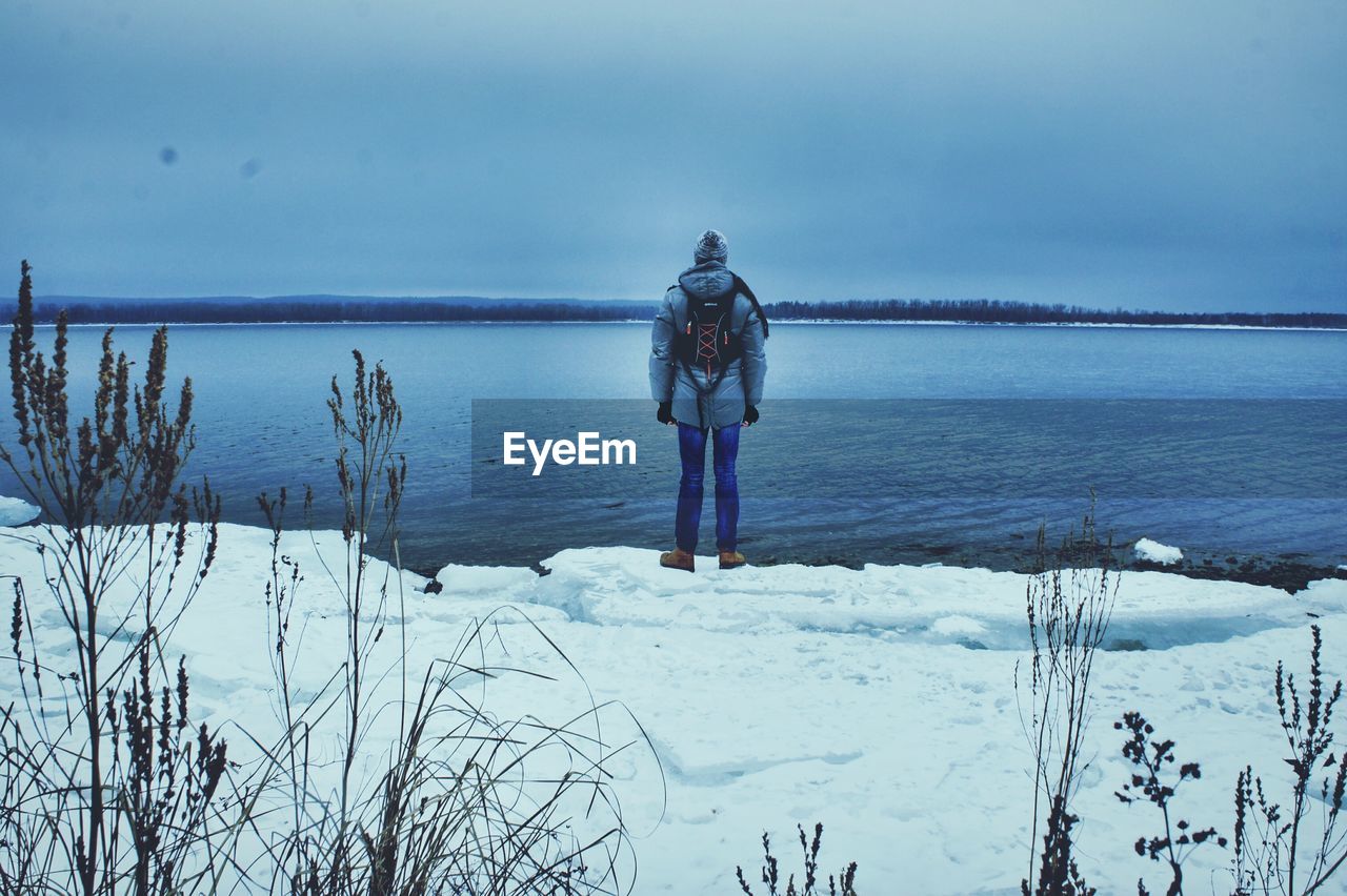 Rear view of man standing on snow covered riverbank