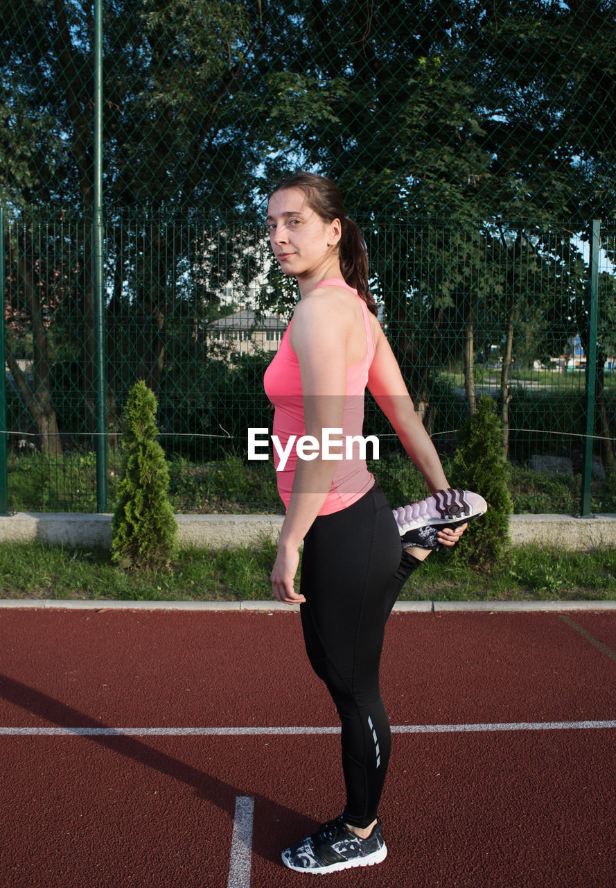 Full length portrait of female athlete stretching on track an field
