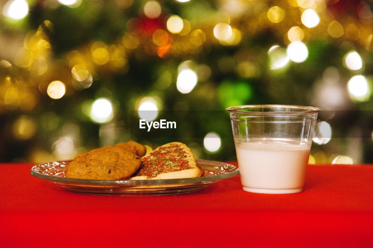 Close-up of drink and cookies on table against illuminated christmas tree