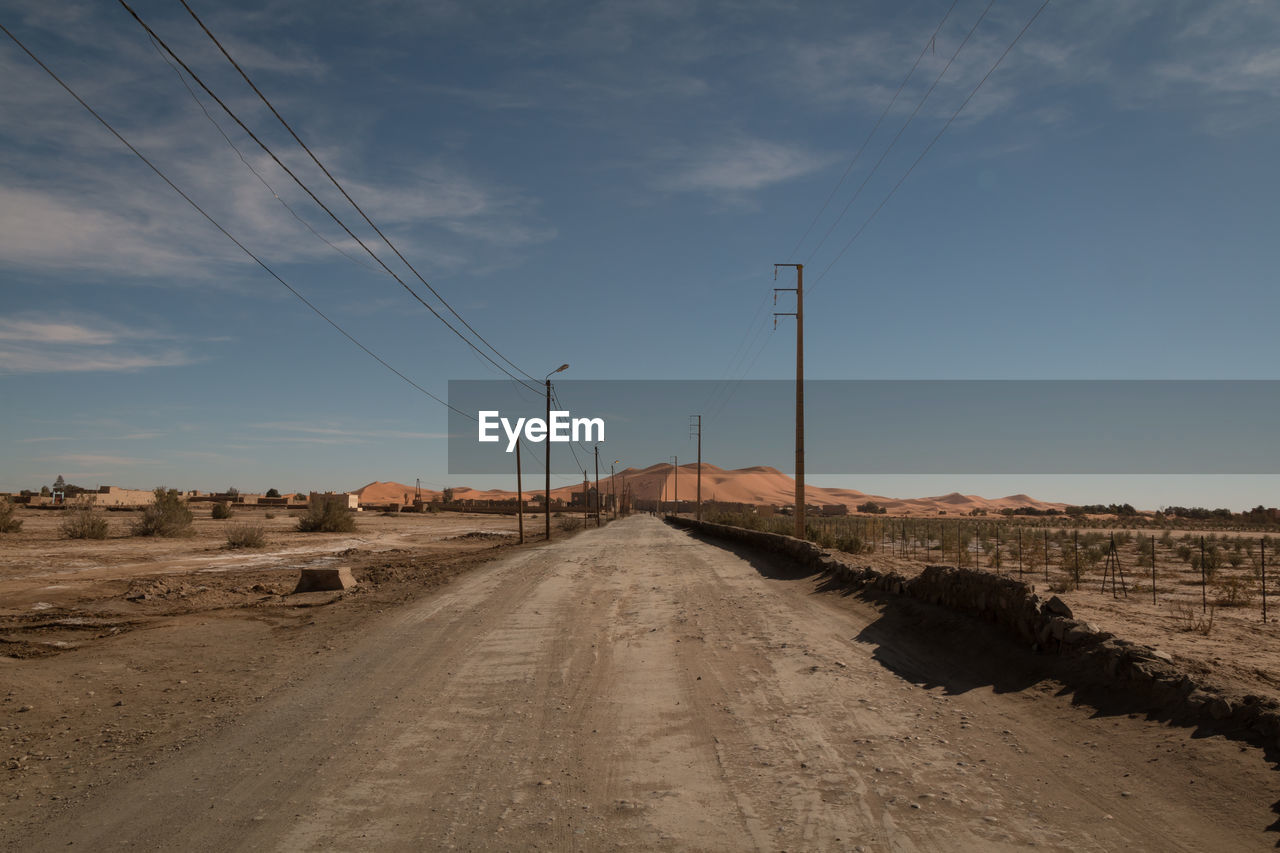 Dirt road and electricity pylons against blue sky