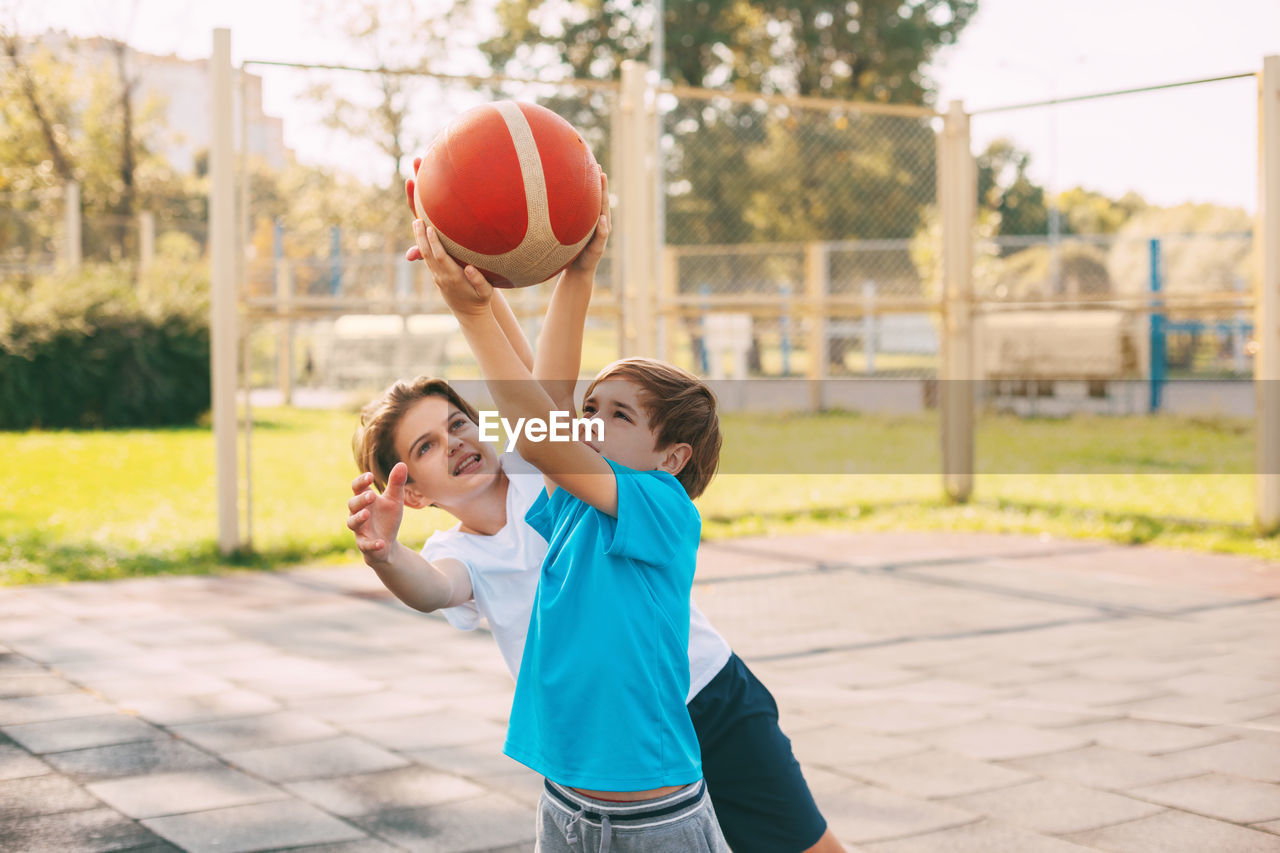 Brothers playing basketball in court