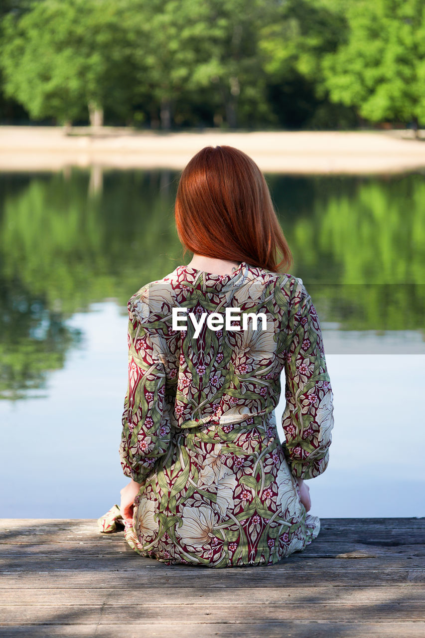 Young woman sitting on wooden pier looking at lake