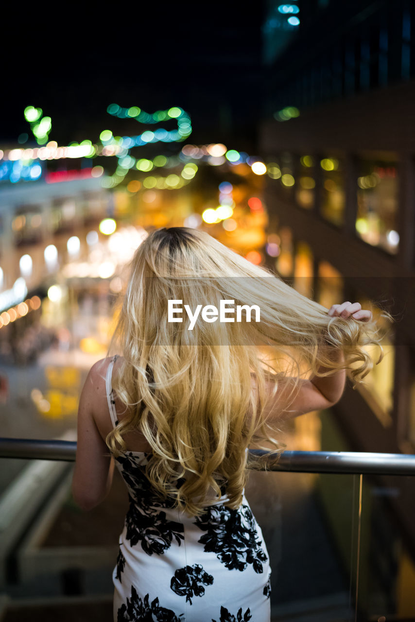 REAR VIEW OF WOMAN IN ILLUMINATED CITY