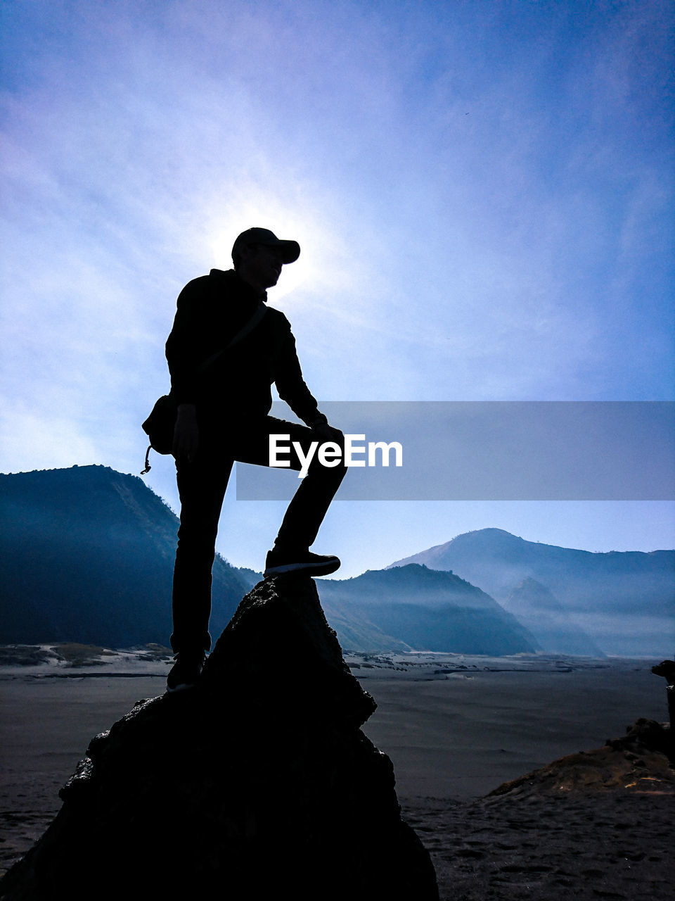 MAN STANDING ON ROCK AGAINST MOUNTAIN