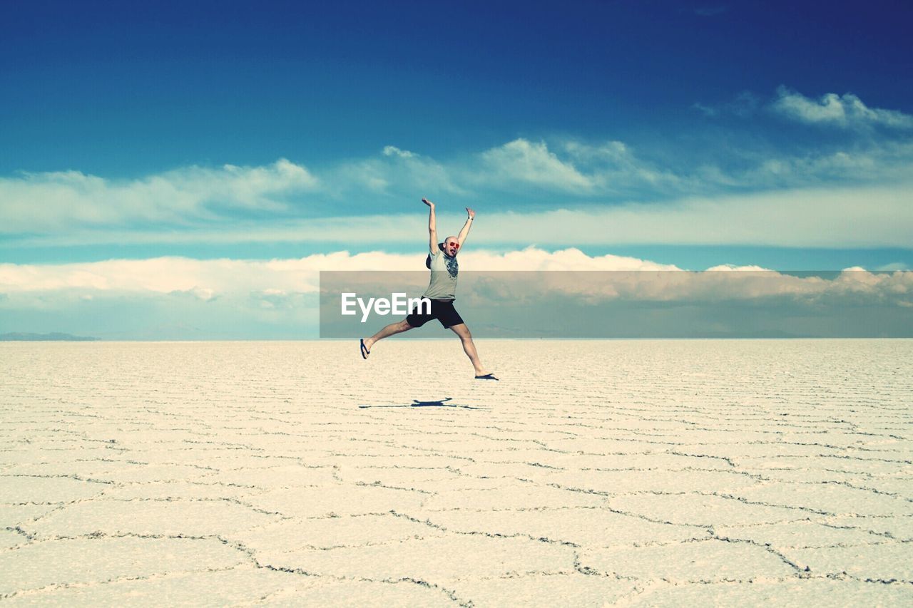 Full length of man with arms raised at salar de uyuni against sky