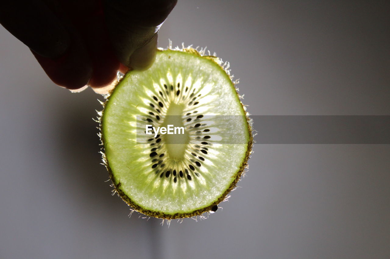 Cropped hand holding kiwi slice against wall