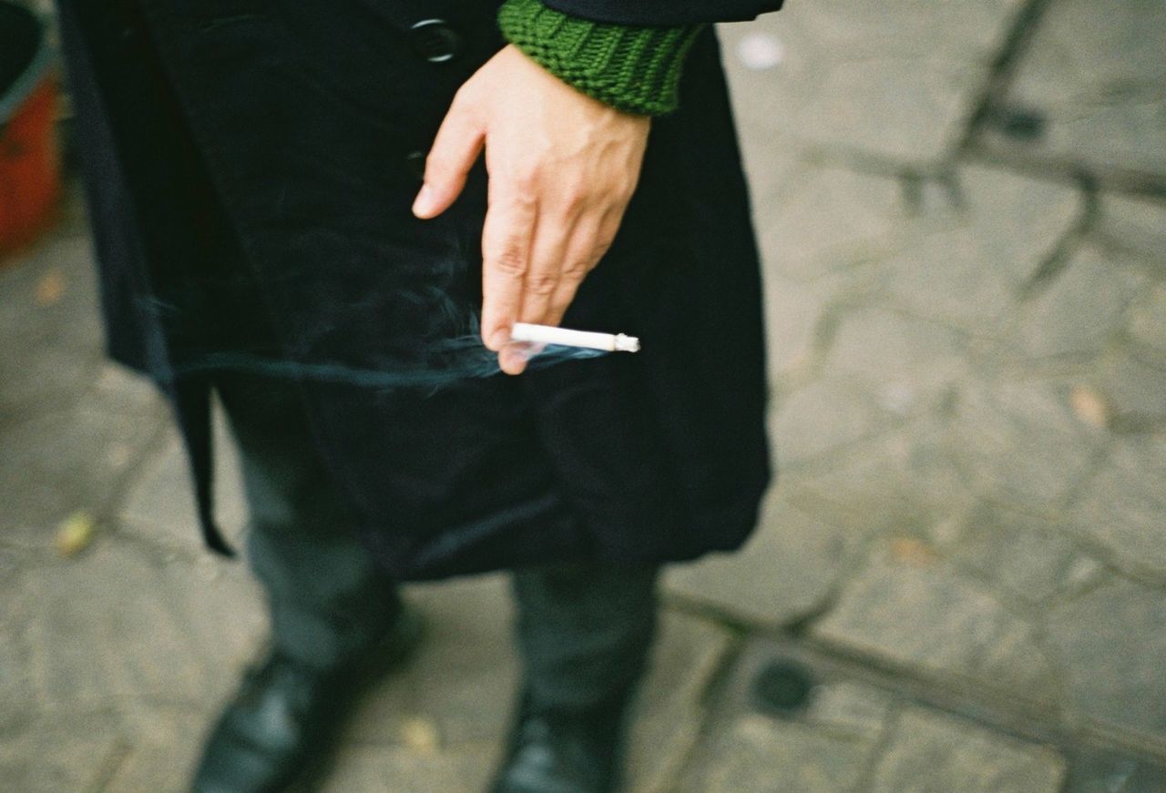 Low section of person holding cigarette on footpath