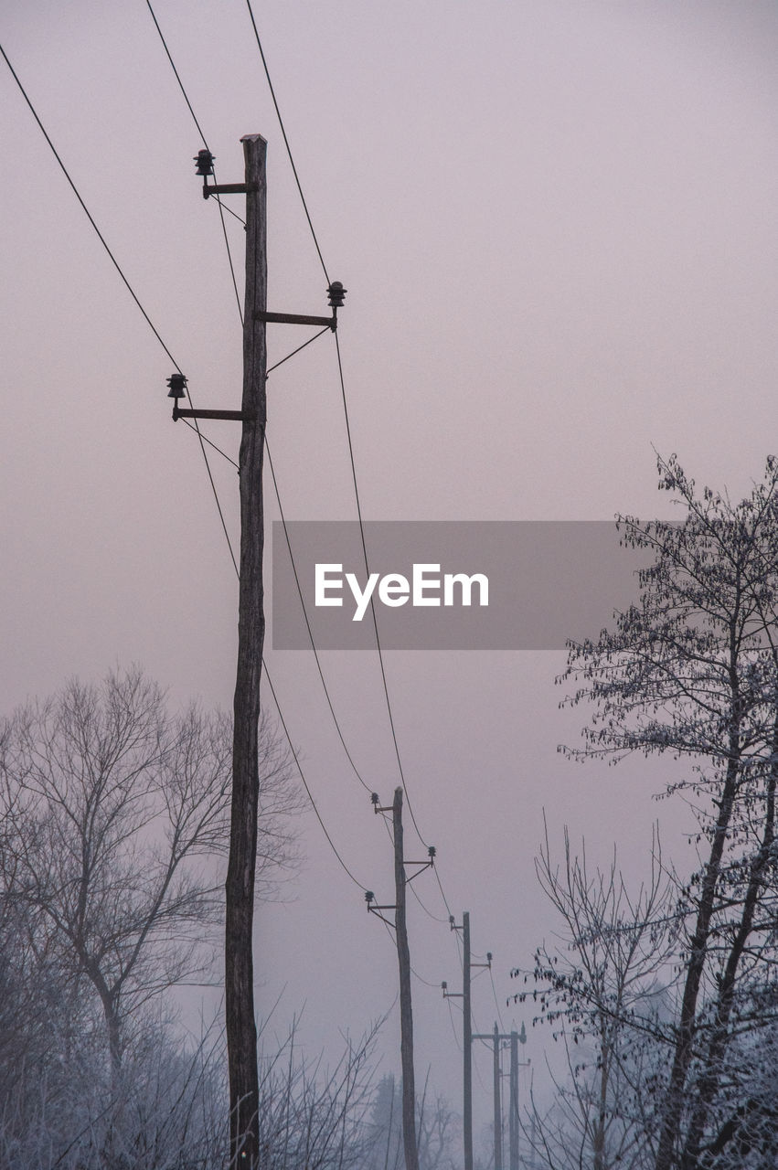 Old wooden electricity pylon in misty winter landscape