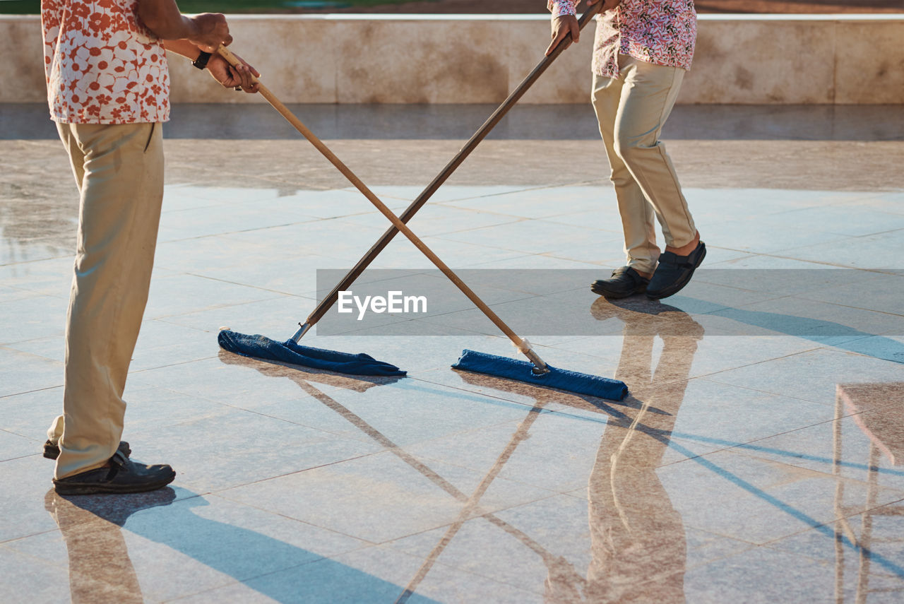 Low section of people cleaning tiled floor