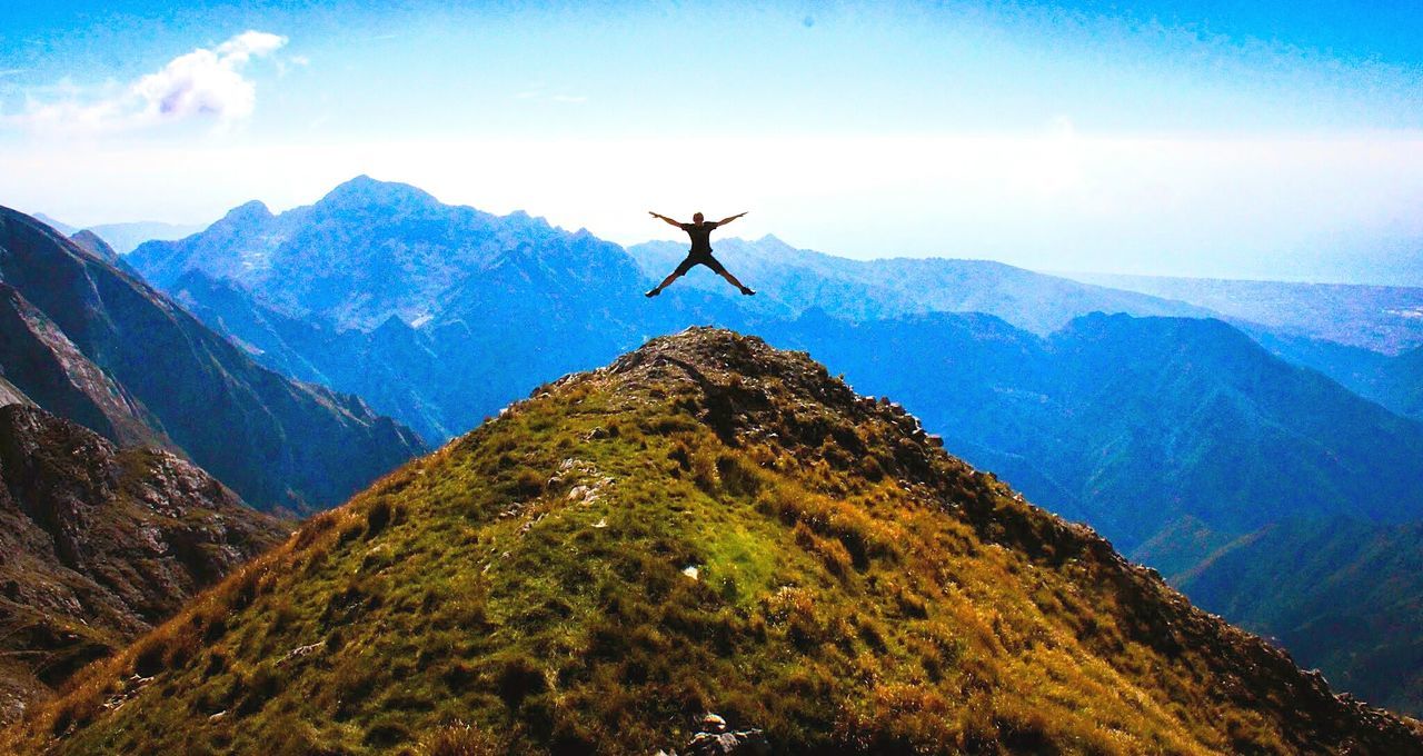 Man jumping over mountains against sky on sunny day