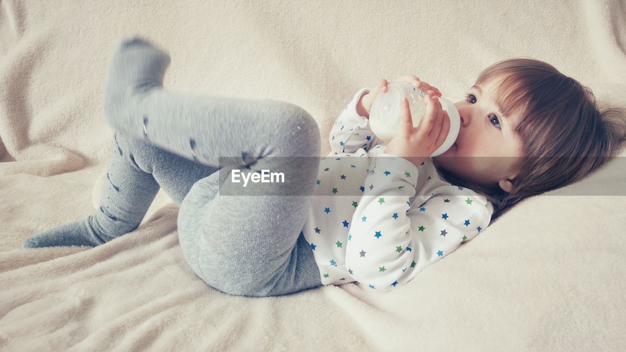 High angle view of girl drinking milk from bottle while lying on bed at home