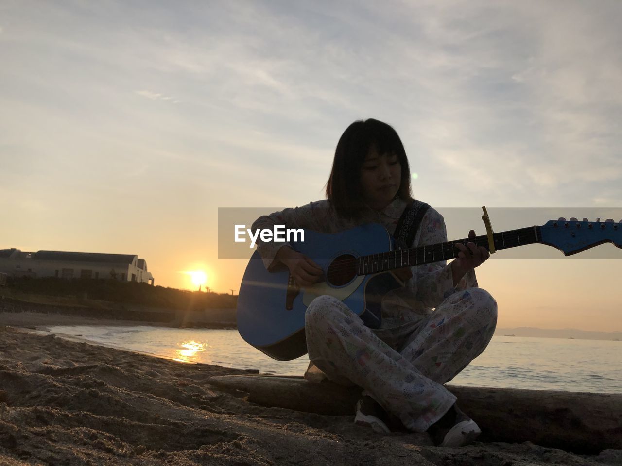 Woman playing guitar at beach against sky during sunset