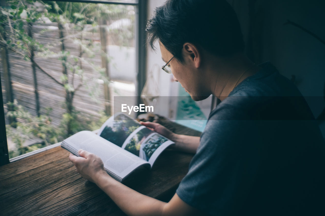 Side view of man reading book at home