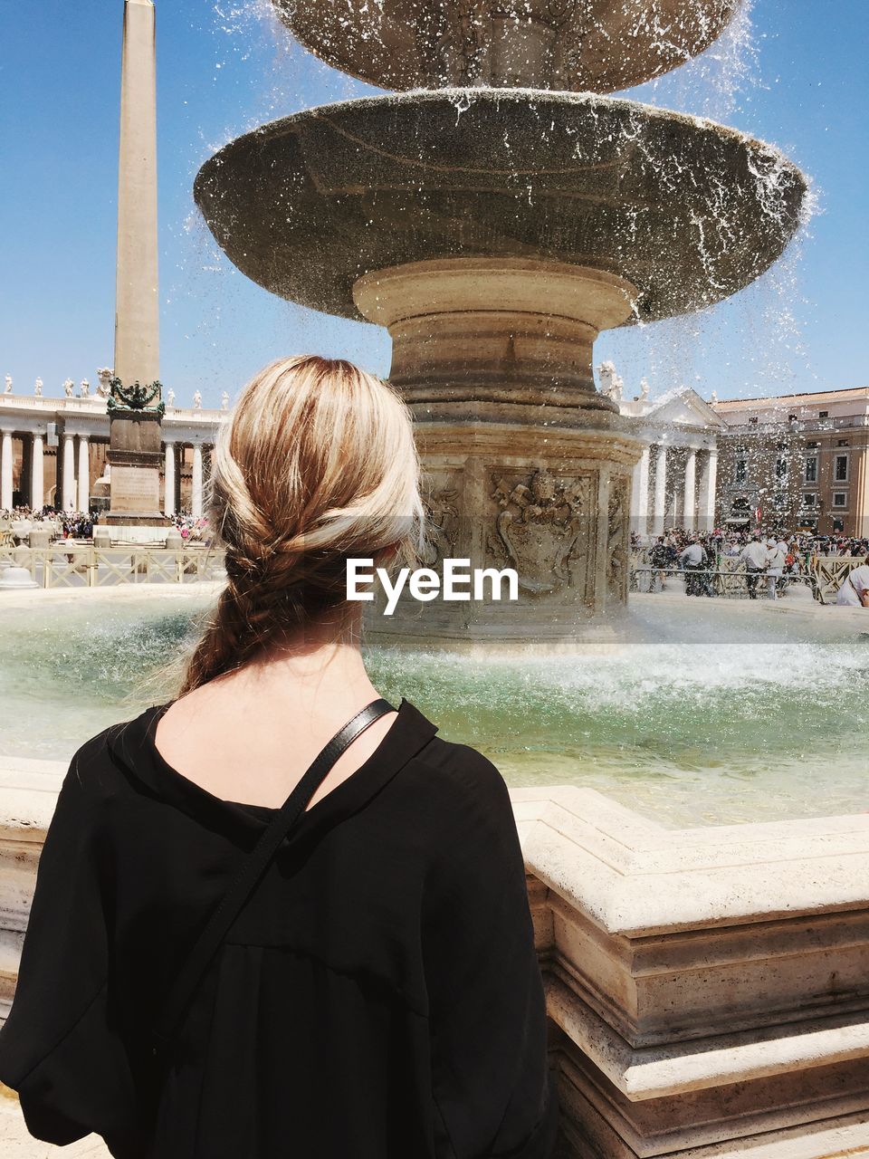 Rear view of woman standing in front of fountain in city