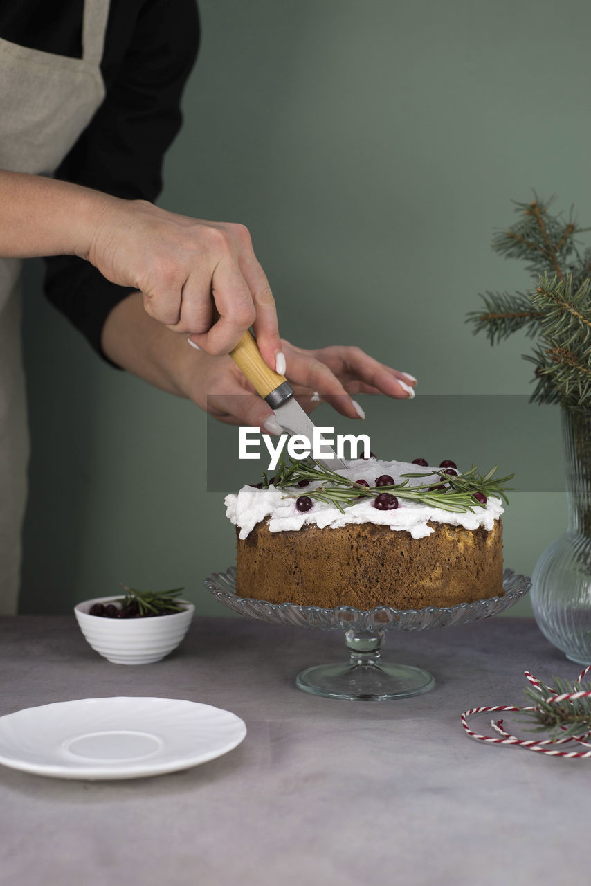 The girl's hands are cutting the christmas cake with red berries on a gray table.