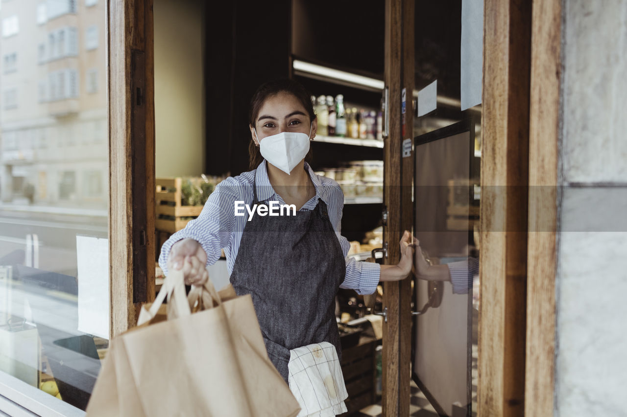 Portrait of female owner with take away food at doorway of delicatessen shop