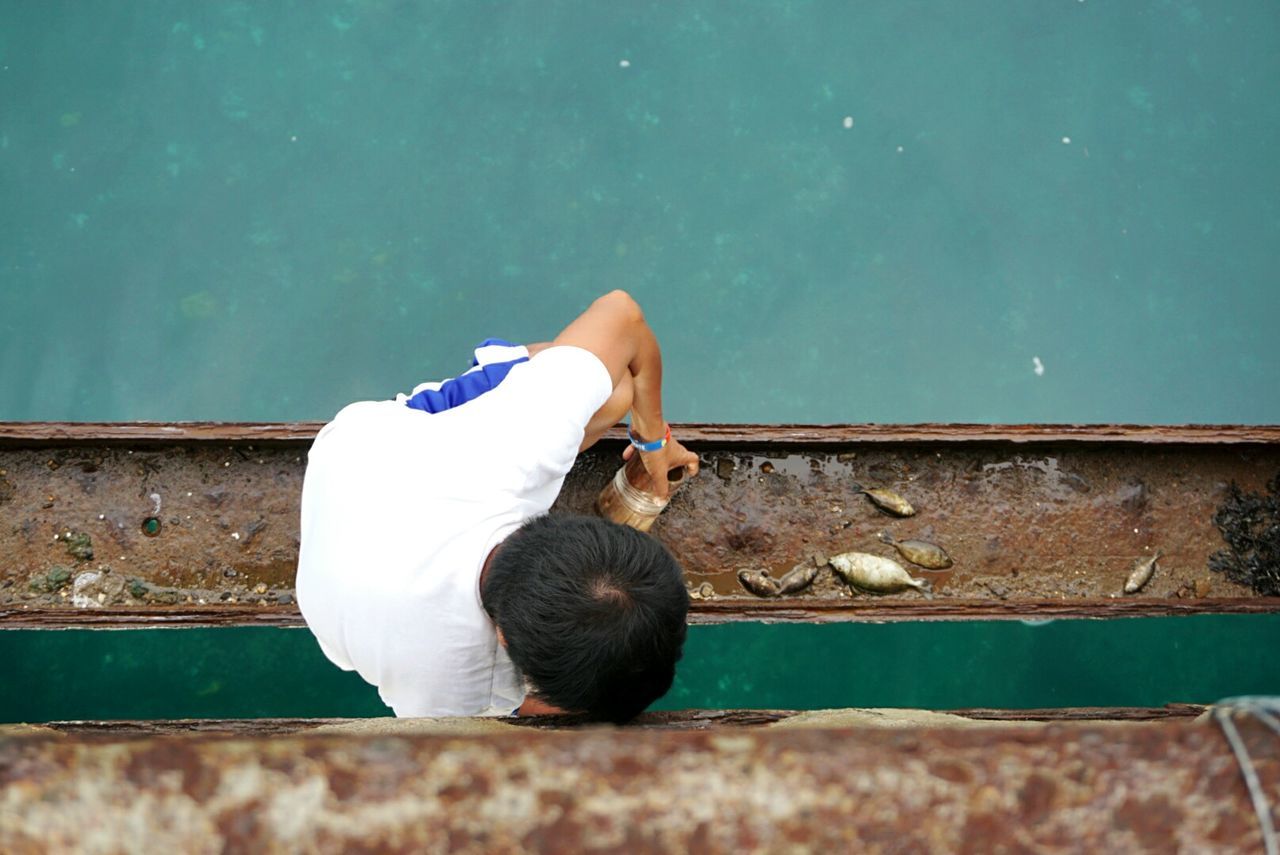 Directly above shot of boy crouching on girder over sea