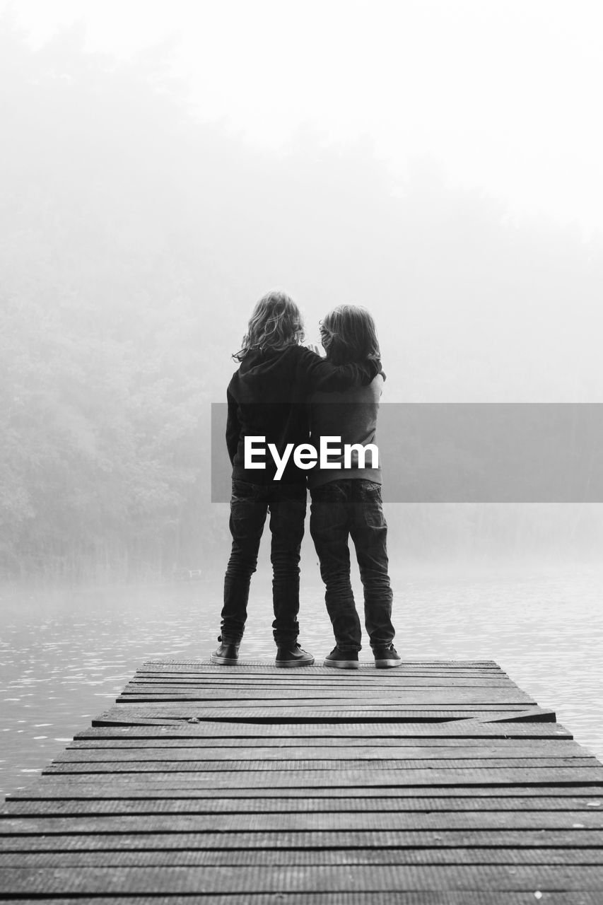 Rear view of siblings on pier over lake during foggy weather