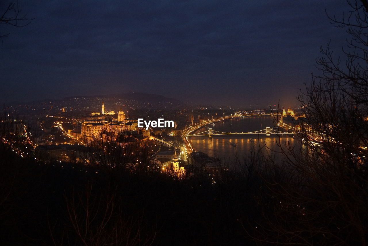 Illuminated cityscape by river against sky at night