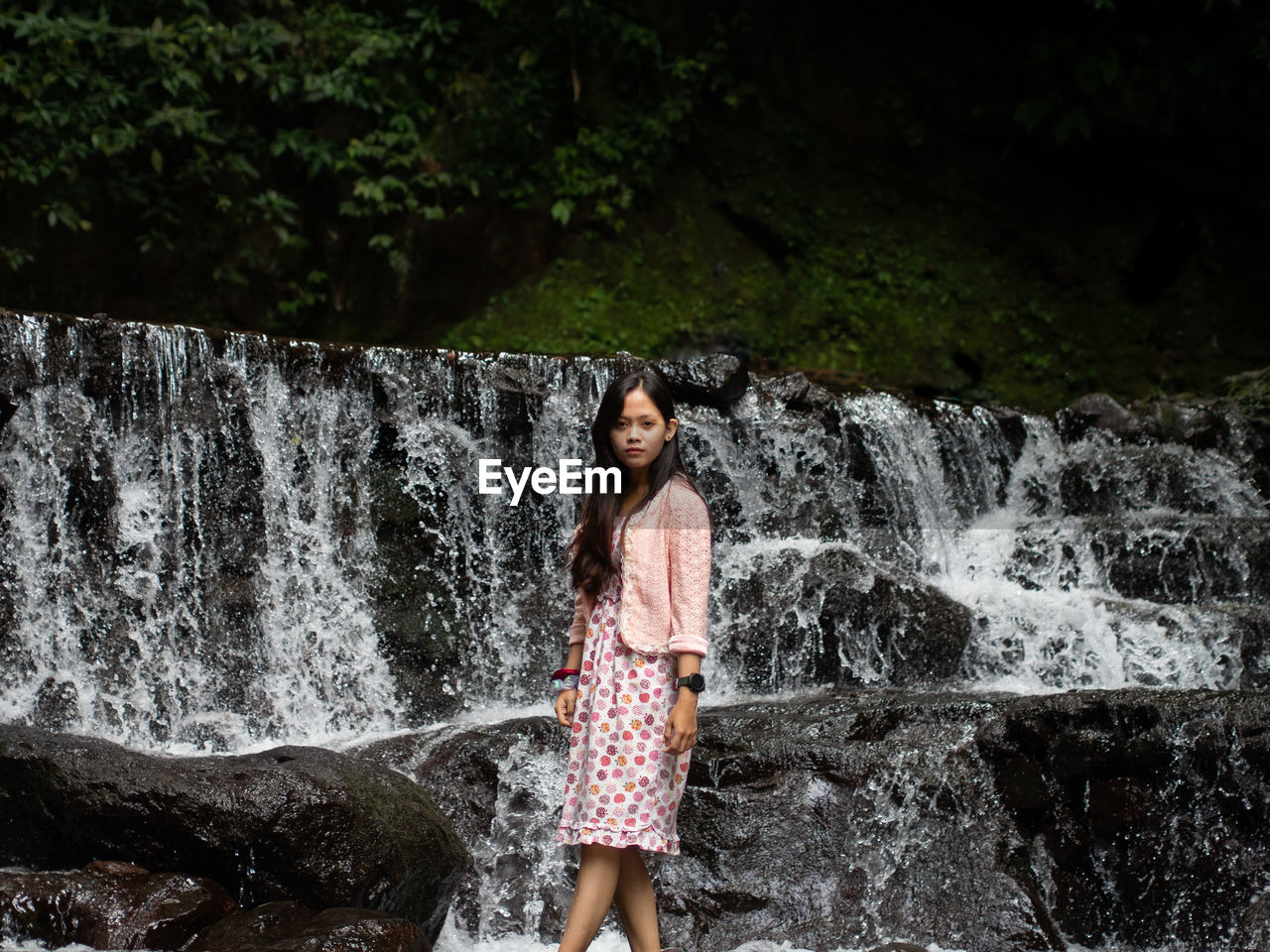 Young woman in pink dress standing against waterfall