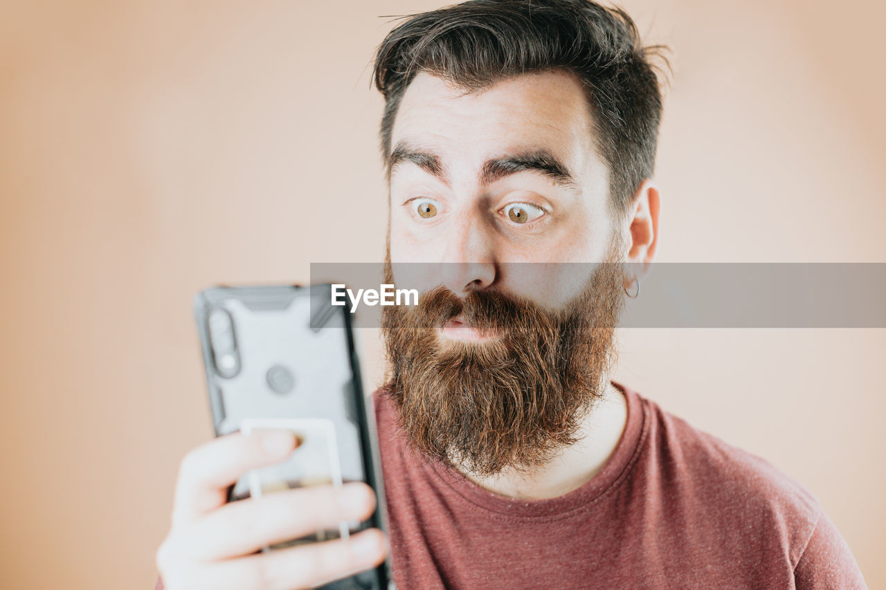 portrait of young man using mobile phone against wall