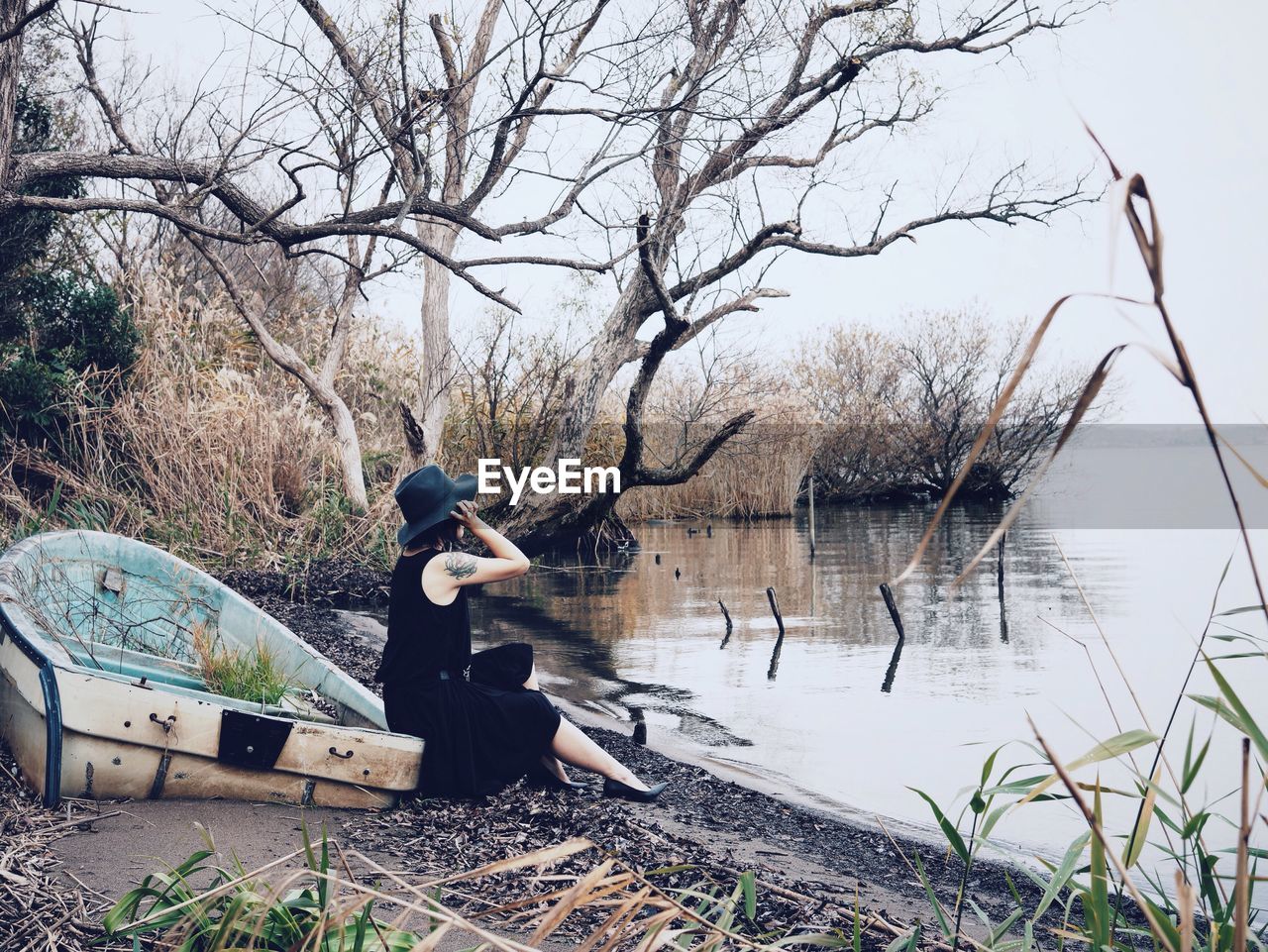 Side view of woman sitting by lake in forest