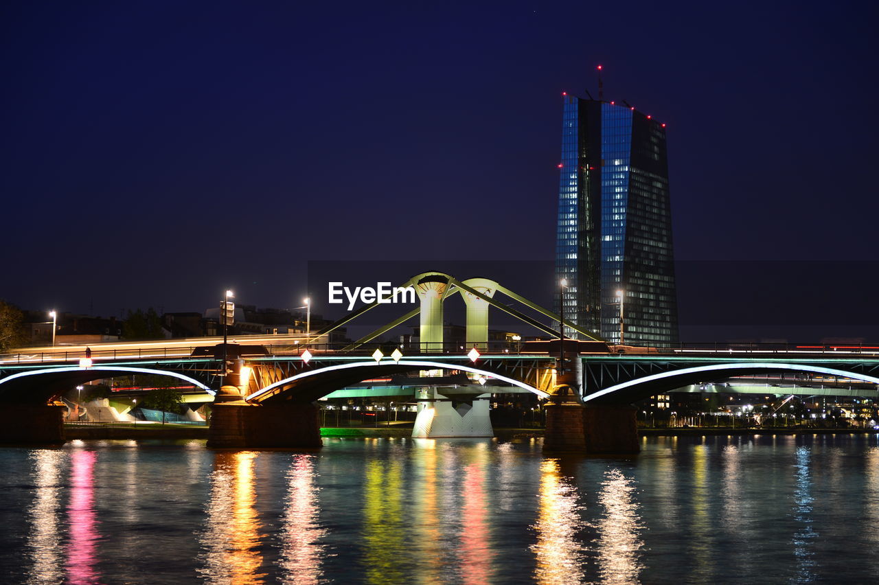 Illuminated bridge over river against sky in city at night