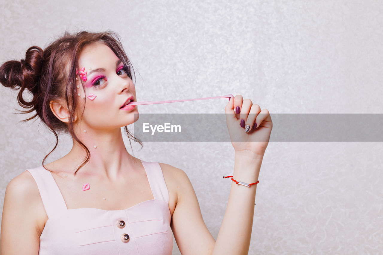 Young woman with pink make-up chewing gum against wall