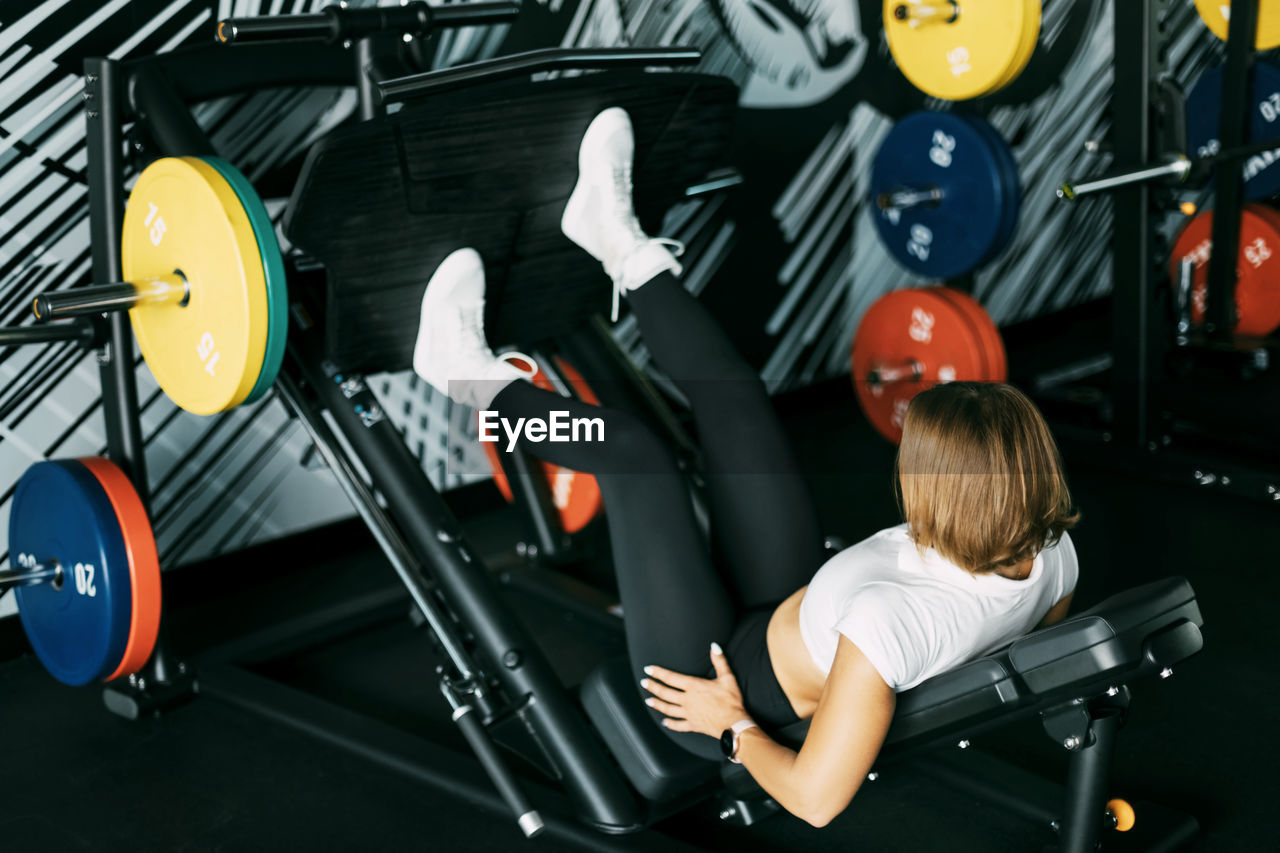 A young woman does exercises for her legs and buttocks while lying on a modern simulator in the gym. 
