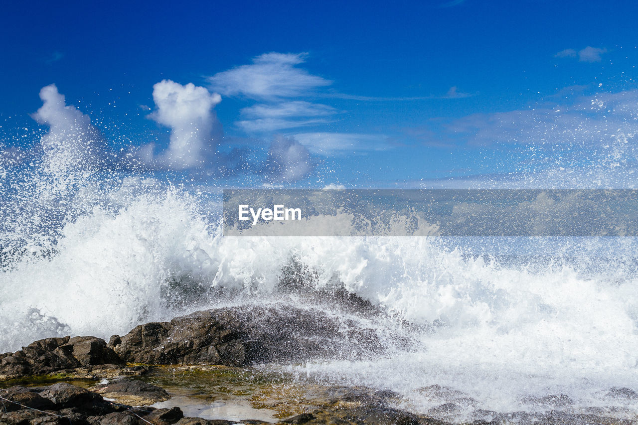 Waves splashing on rocks against sky