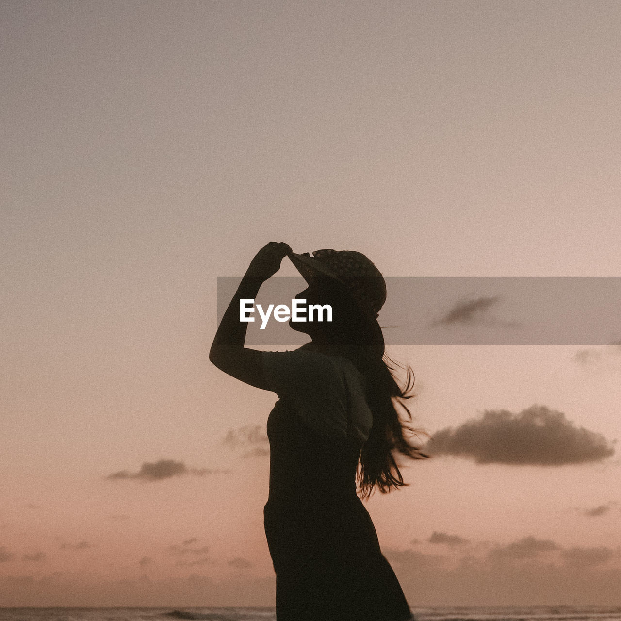 Silhouette woman with arms raised standing against sky during sunset