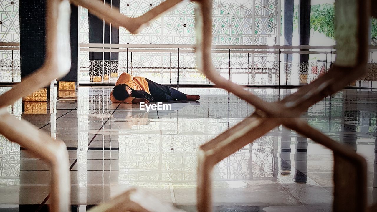 Man lying on tiled floor seen from metal grate