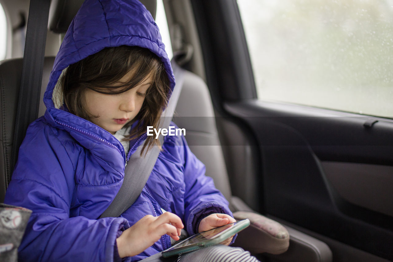 A small child travels in a car looking at a cell phone screen on trip