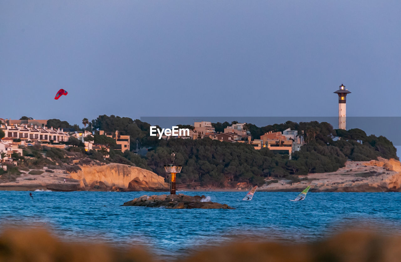 LIGHTHOUSE AMIDST BUILDINGS AGAINST SEA