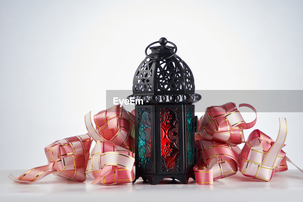Close-up of traditional arabic lantern and ribbon ketupat against white background