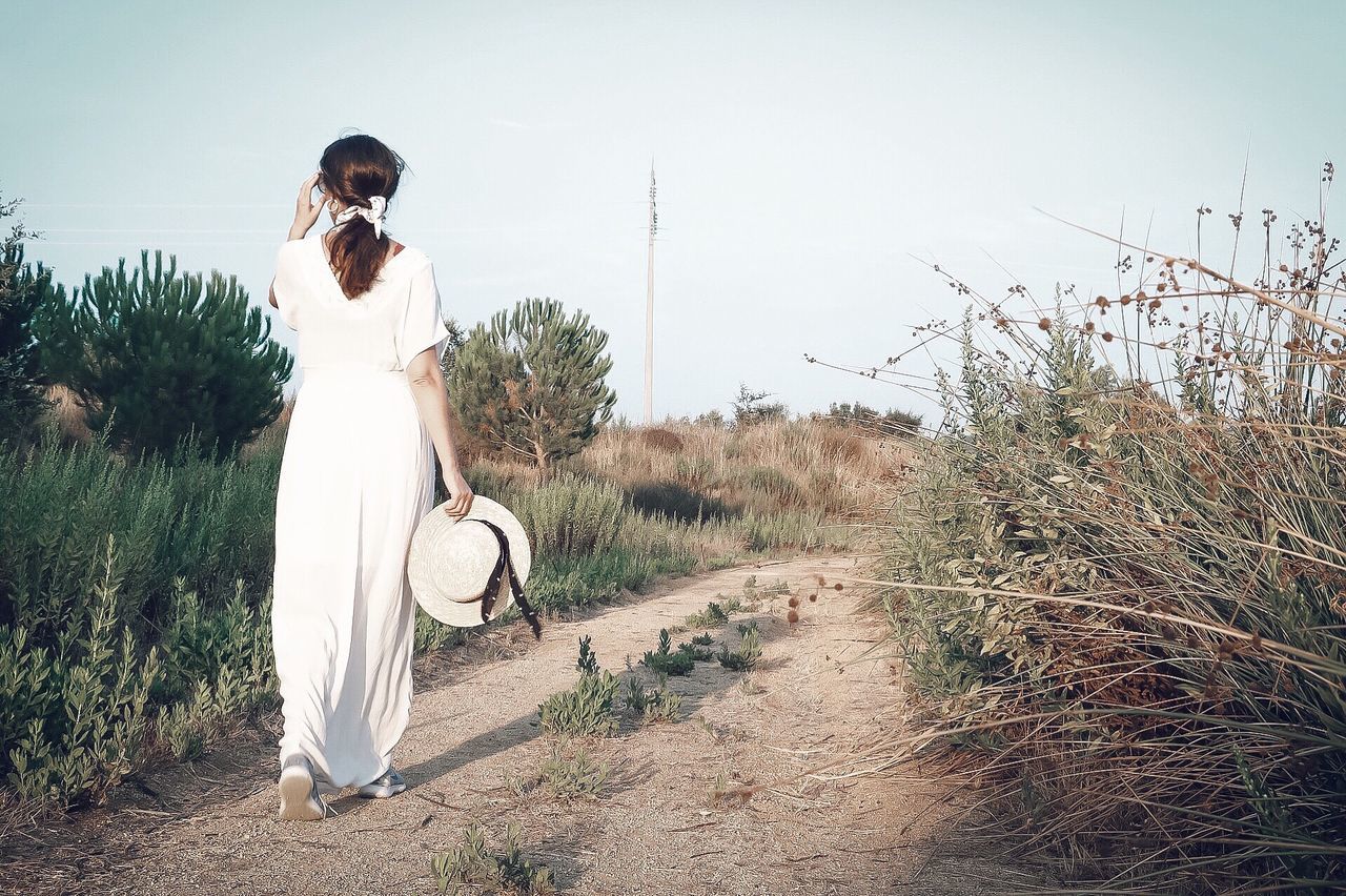 Full length rear view of woman walking by plants against sky