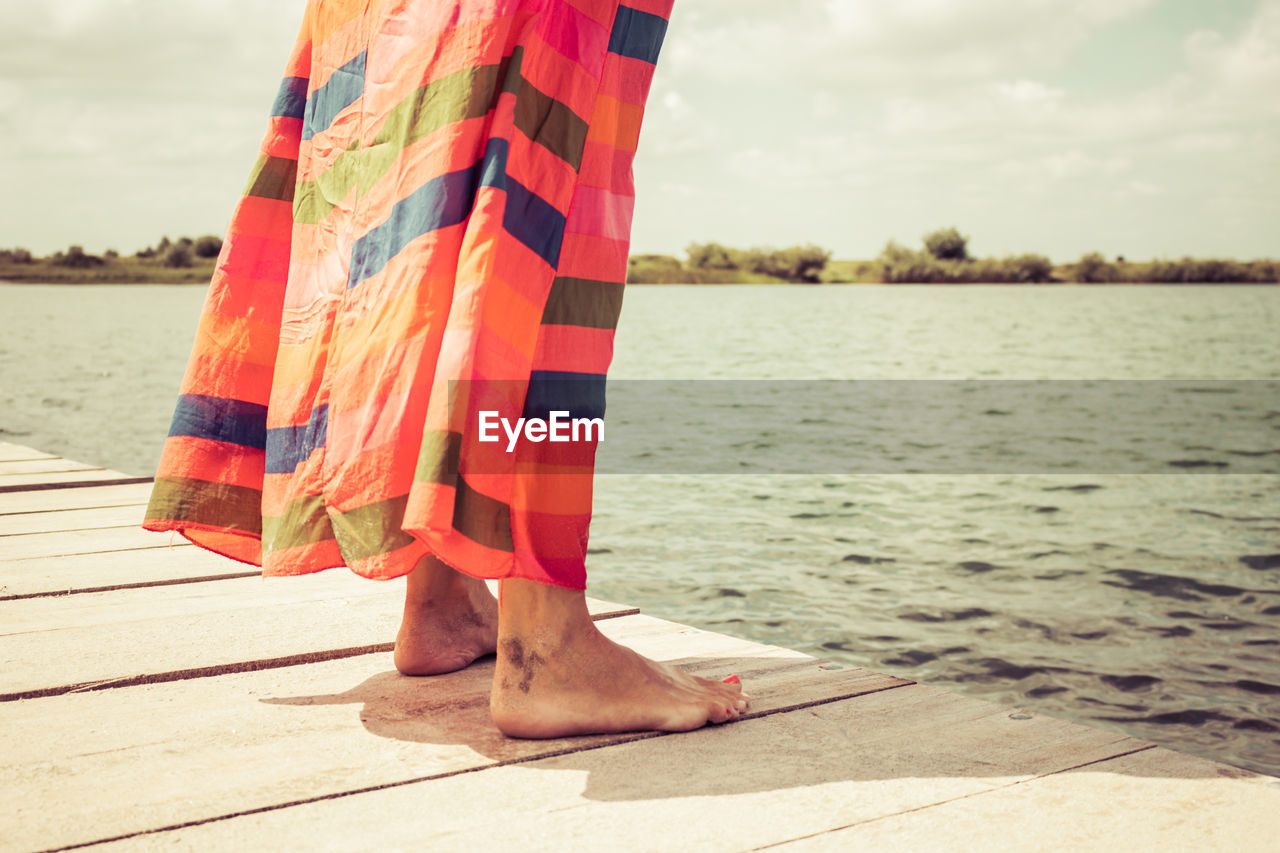 Low section of woman standing on pier during sunny day