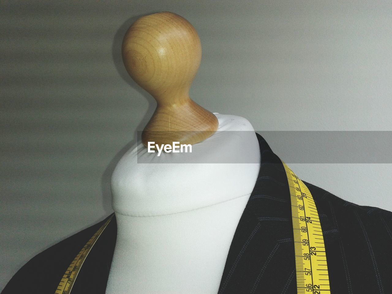 Jacket and measuring tape on dressmakers model against white wall