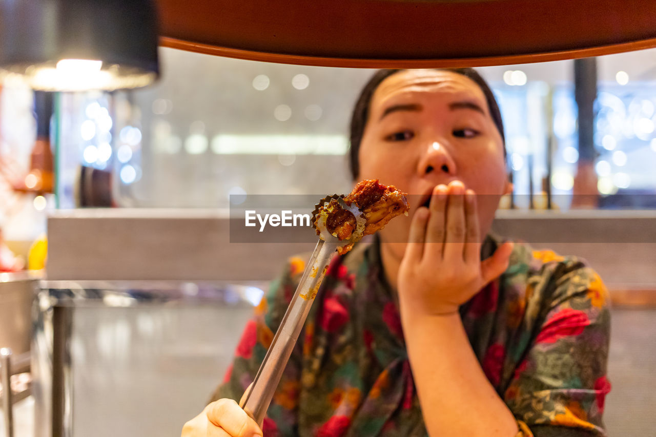 Shocked woman holding food by barbecue grill in restaurant