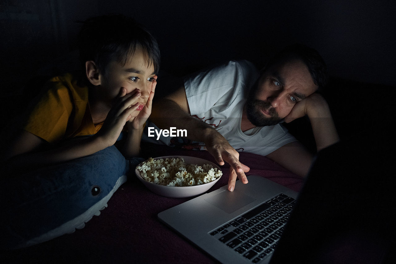 High angle view of boy with father watching movie in darkroom