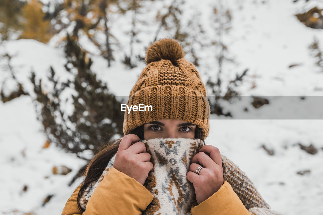 Outdoor winter portrait of young woman wearing winter clothes, holding scarf over her mouth and nose