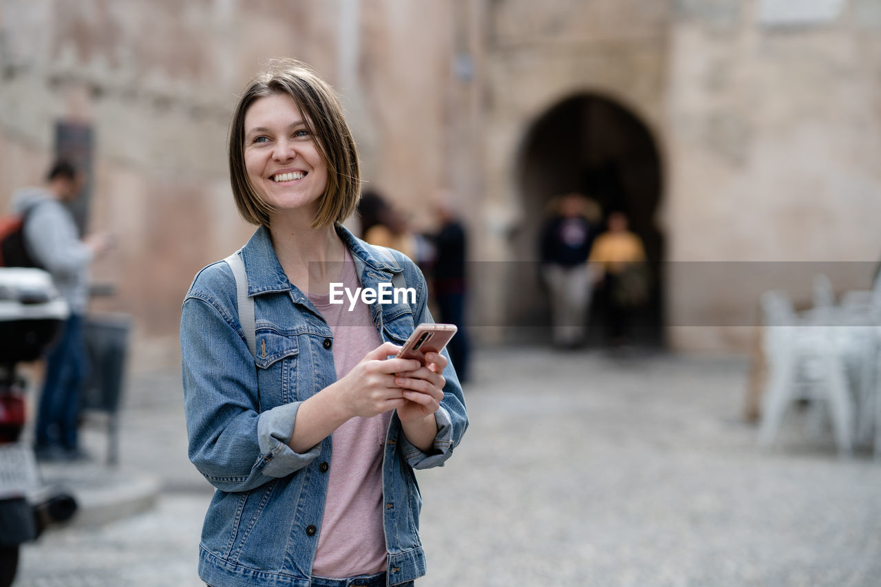Smiling woman using smart phone in city