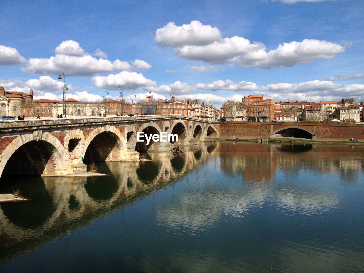 Arch bridge over river by buildings against sky