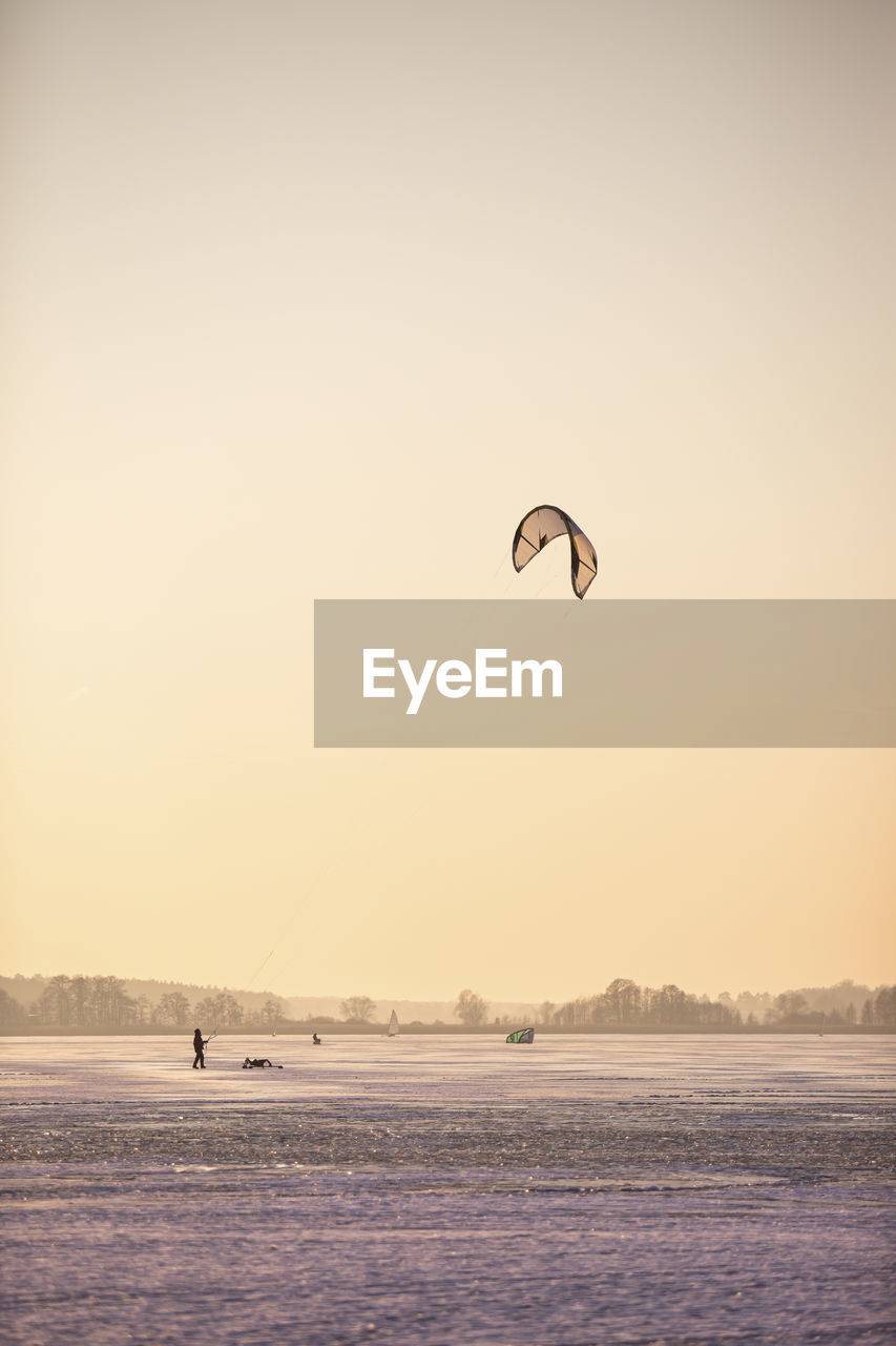Germany, brandenburg, rangsdorf, winter landscape with frozen lake, people playing with kite