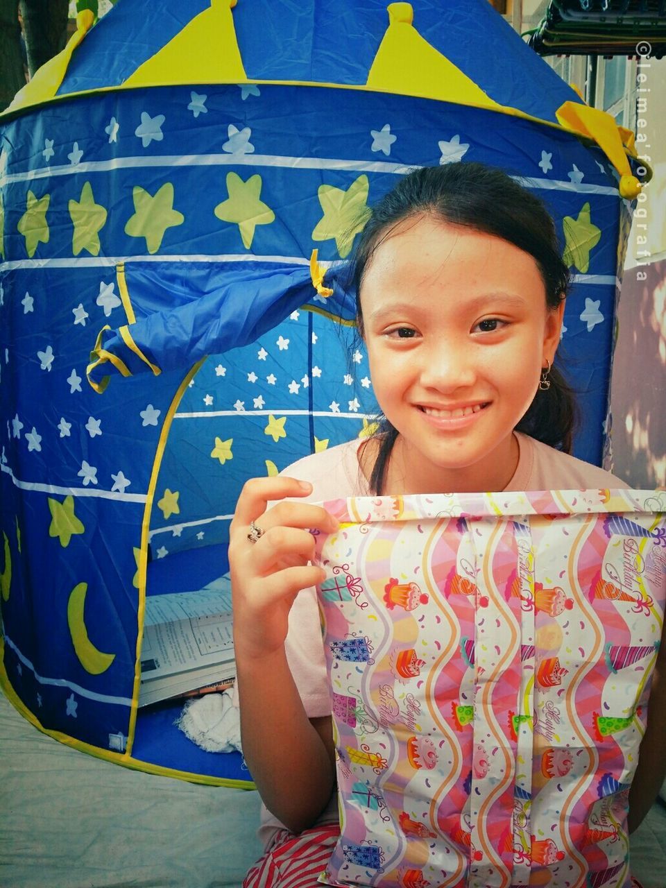 Portrait of smiling teenage girl holding gift against tent