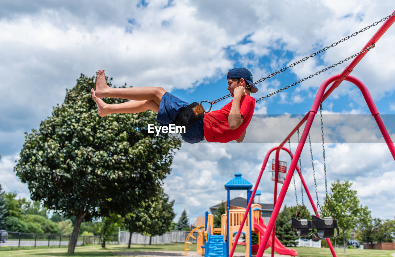 Side view of boy on a swing with playground in the background.