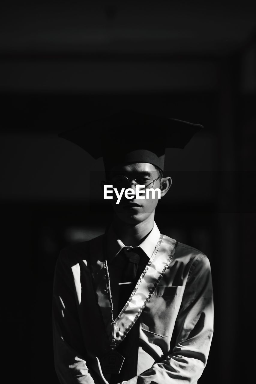 Portrait of young man standing against dark