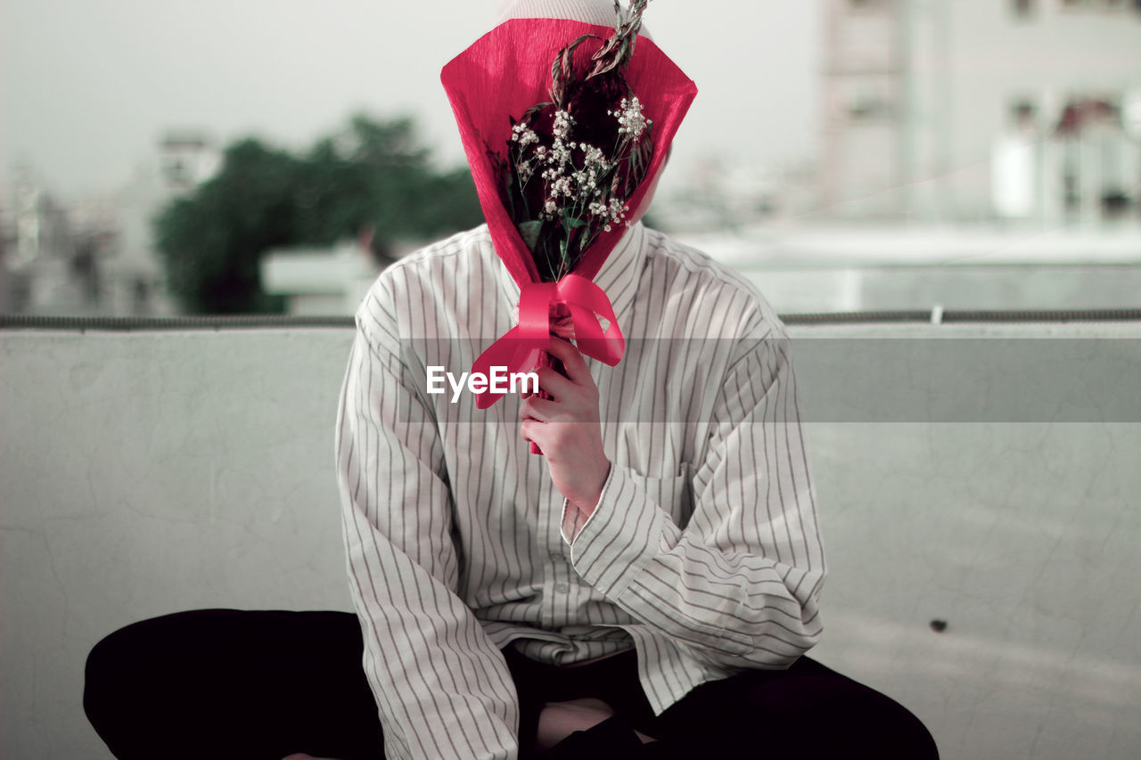 Close-up of man covering face with bouquet