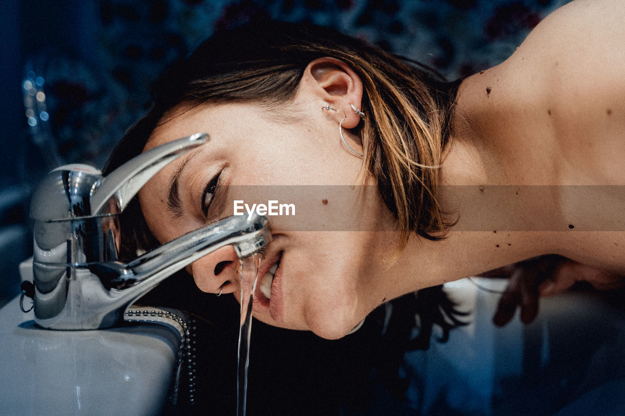 Close-up portrait of woman drinking water from faucet in sink