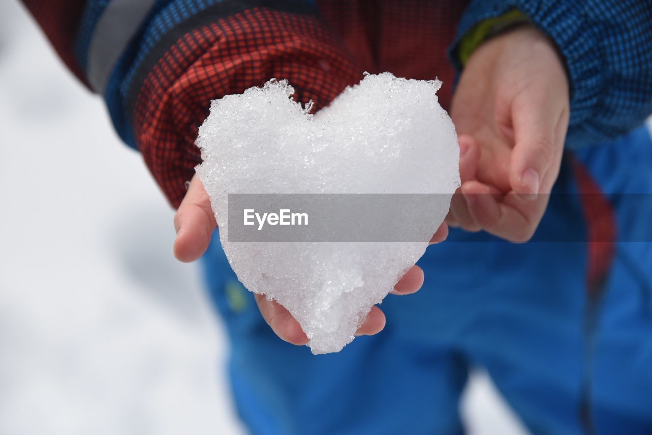 Midsection of man holding snow forming heart shape
